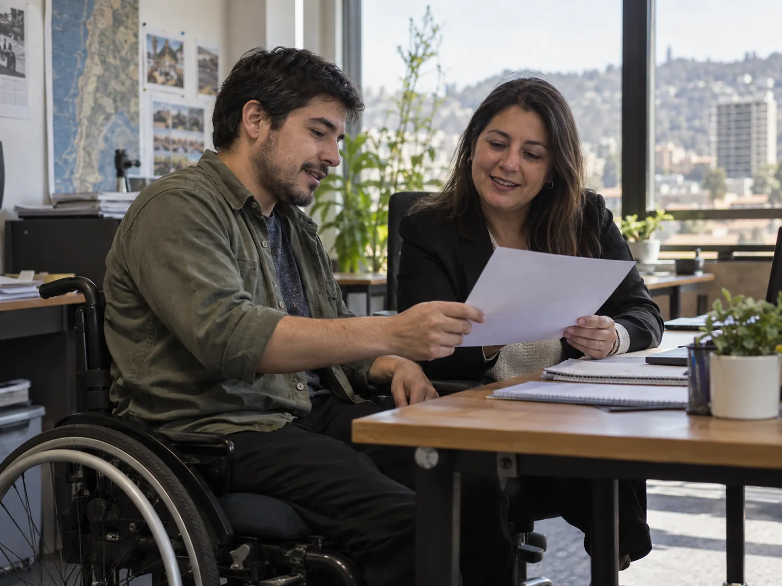 Gestora de inclusión revisando un plan de trabajo con un colega en silla de ruedas